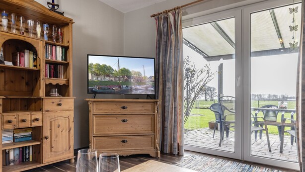 Ein Zimmer mit einem Bücherregal aus Holz, einem Fernseher und Blick auf eine Außenpatio mit Stühlen und einem Tisch.