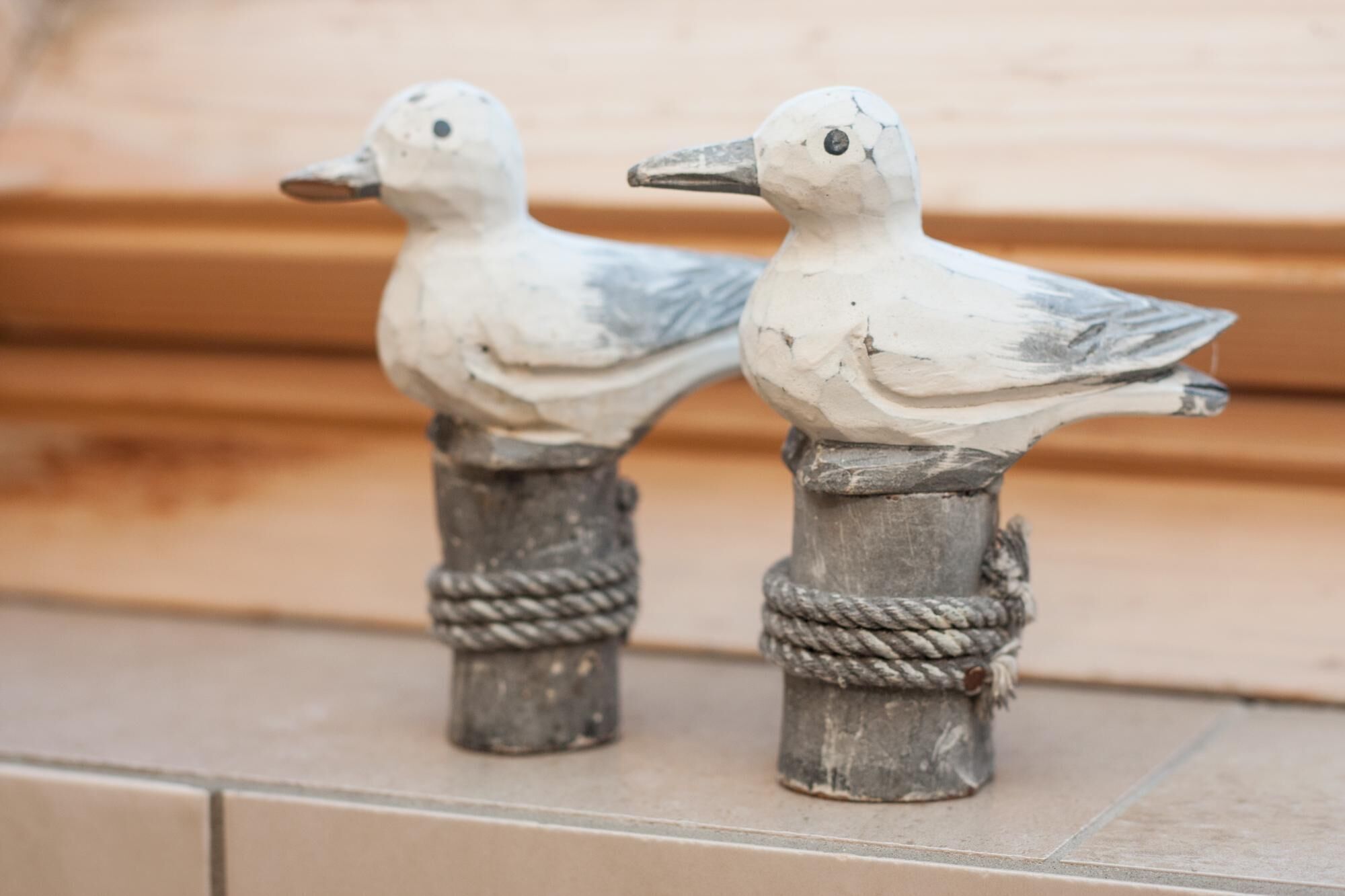 Deux sculptures en forme d’oiseaux, ornées de motifs en forme de corde, sont posées sur une surface carrelée.