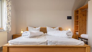 Ein ordentlich bezogenes Bett mit weißen Leinen und Kissen, ein hölzerner Kopfteil und ein Nachttisch mit Lampe.