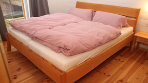 Un lit en bois avec une couverture à carreaux et des oreillers, une table de chevet en bois et une fenêtre avec des rideaux.