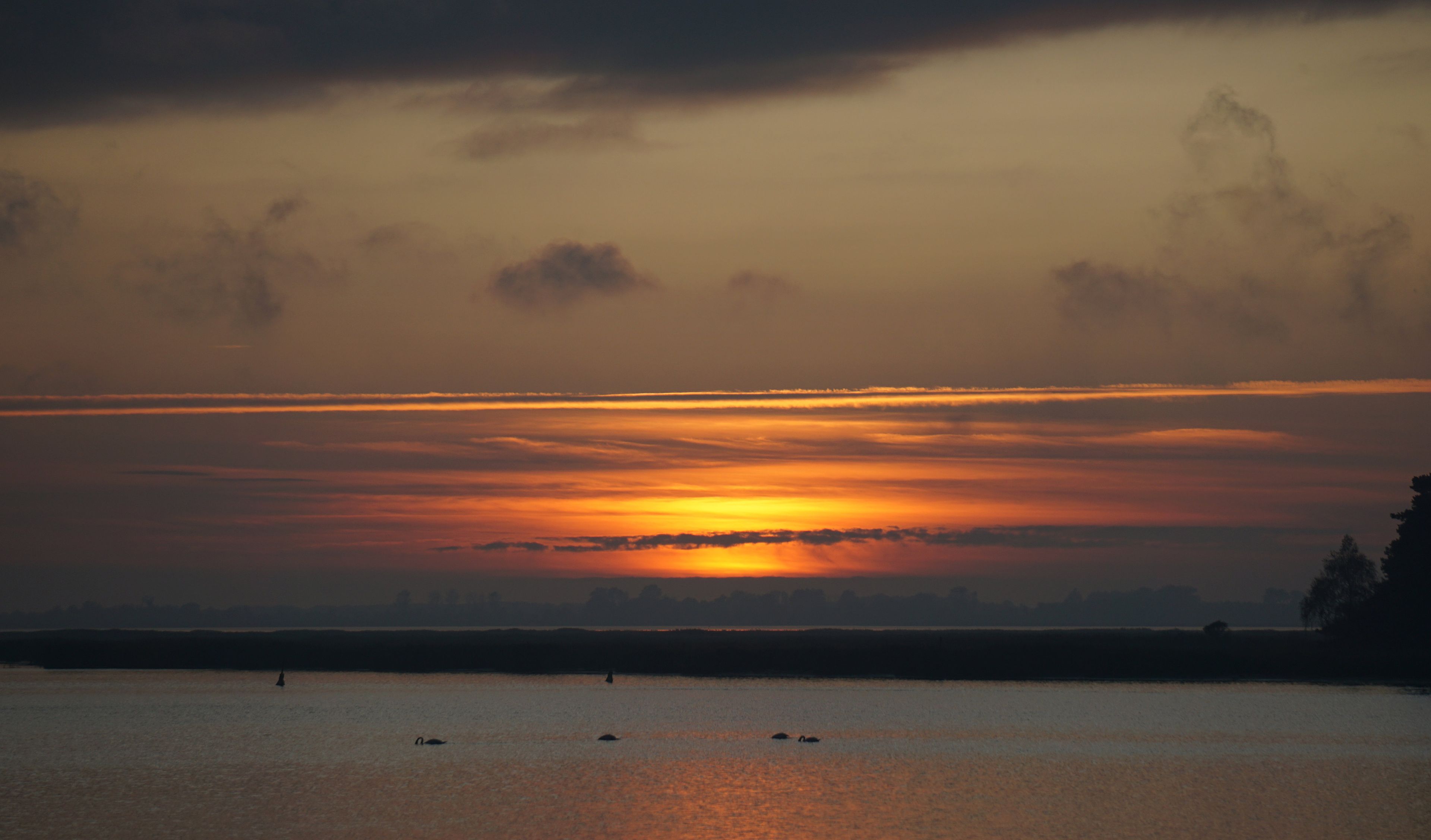 Un coucher de soleil sur une étendue d’eau calme, avec des bateaux.