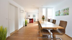 A spacious room with a long wooden dining table, wicker chairs, and a kitchen in the background. - Old Town Apartment "Himmelreich" (Heidelberg)