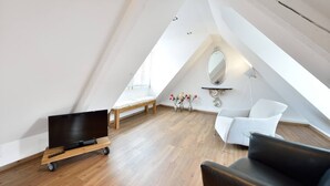 A modern loft bedroom with a sloped ceiling, a wooden bed, a white armchair, a black leather sofa, and a small table with a mirror. - Old Town Apartment "Himmelreich" (Heidelberg)