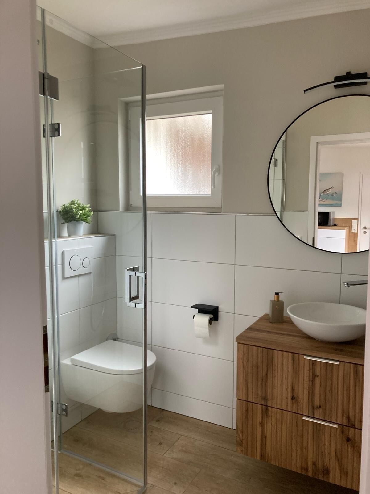 Ein modernes Badezimmer mit Duschkabine aus Glas, Toilette, Waschbecken mit Holzunterschrank und Spiegel.