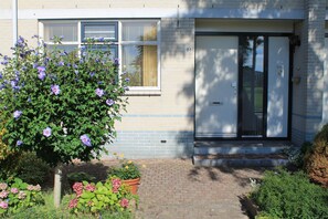 Stroll up the brick pathway to the entrance of this charming home, surrounded by lush flowering plants and a beautiful tree.