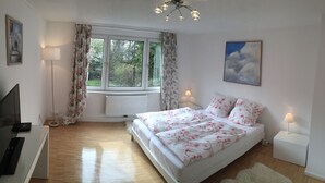 Een slaapkamer met een bed, een bureau, een televisie en een raam met gordijnen.