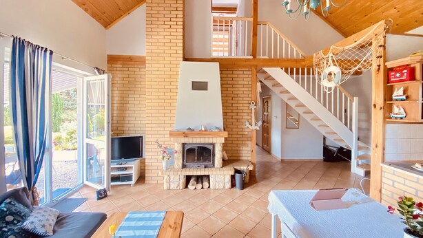 Amplia sala de estar con chimenea, techo de madera y una escalera que conduce a un nivel superior.