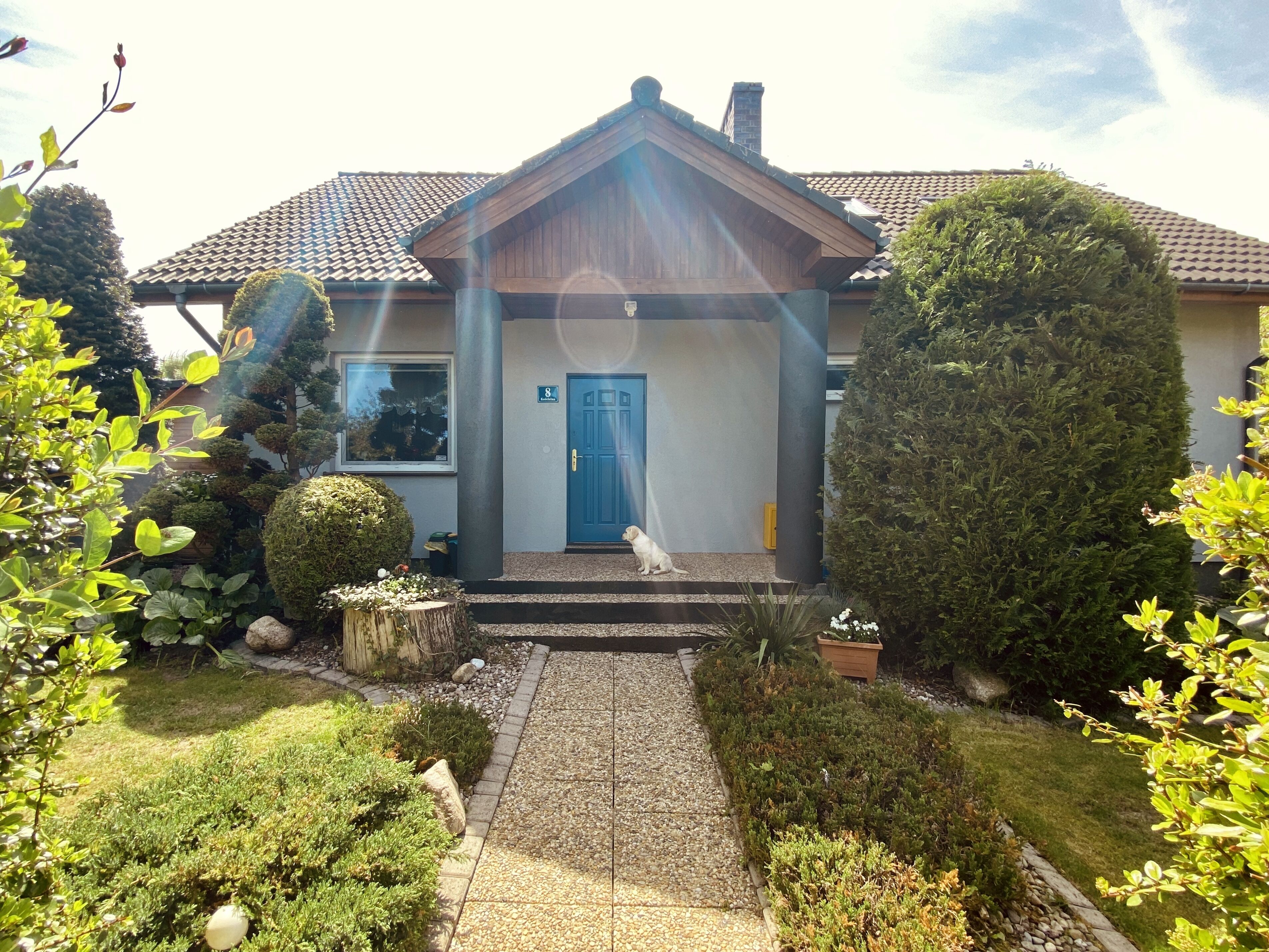 Uma casa com porta azul, um pequeno alpendre e um jardim bem cuidado.
