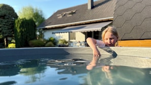 Niño/a inclinado/a sobre una piscina con una casa al fondo.