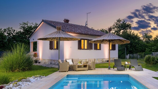 Una casa con piscina, mobiliario exterior y sombrillas.