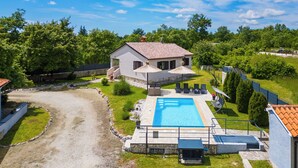 Una casa con piscina, un patio cubierto y un jardín cercado.