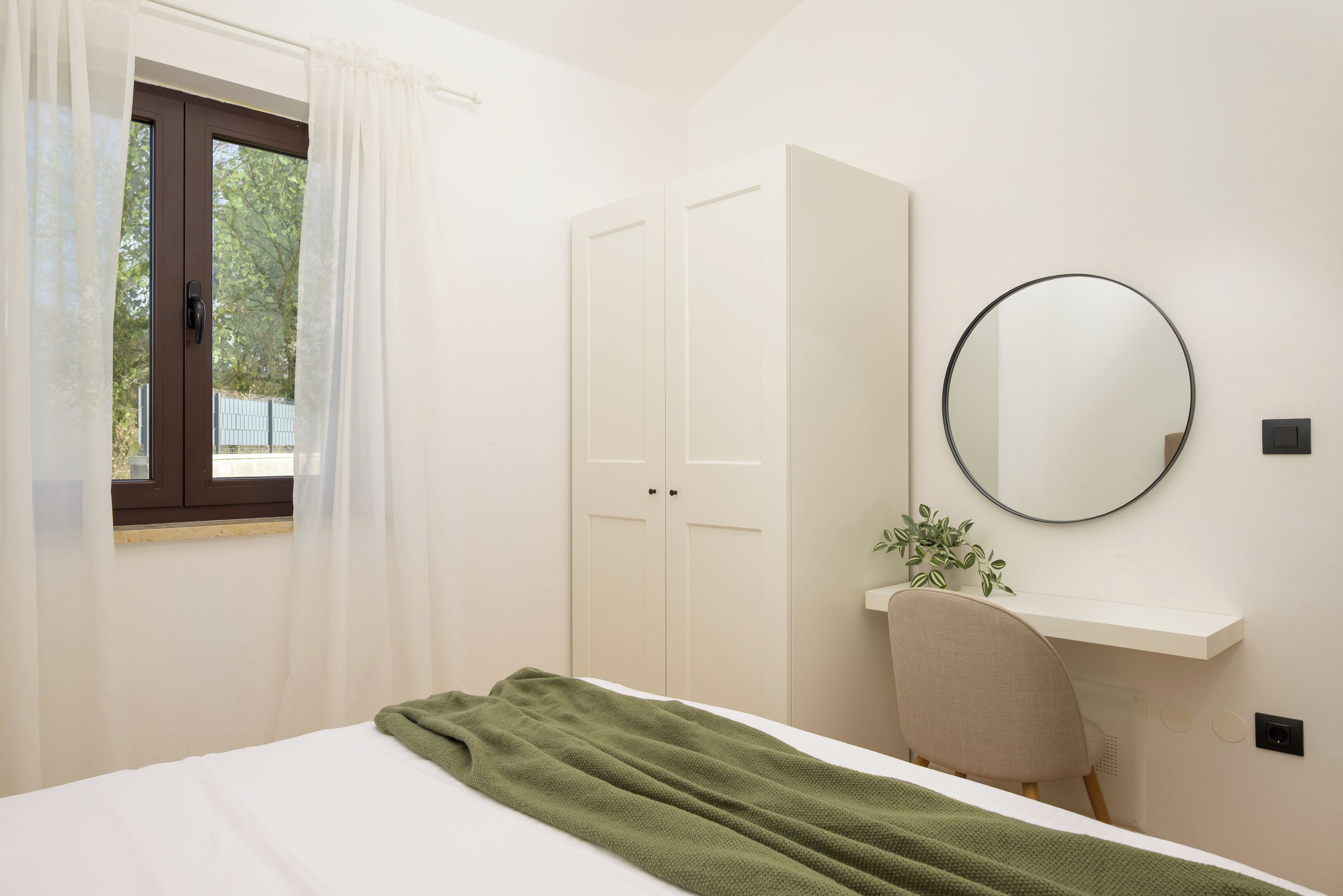 A bedroom with a bed, a desk, a chair, a mirror, and a wardrobe.