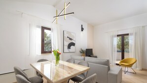Una sala de estar moderna con una mesa de comedor de cristal, sofás grises, un sillón amarillo y un televisor plano negro.