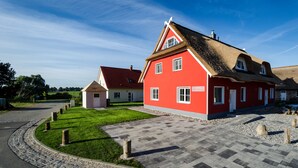 Une maison rouge avec un toit de chaume, une allée pavée et une pelouse bien entretenue.