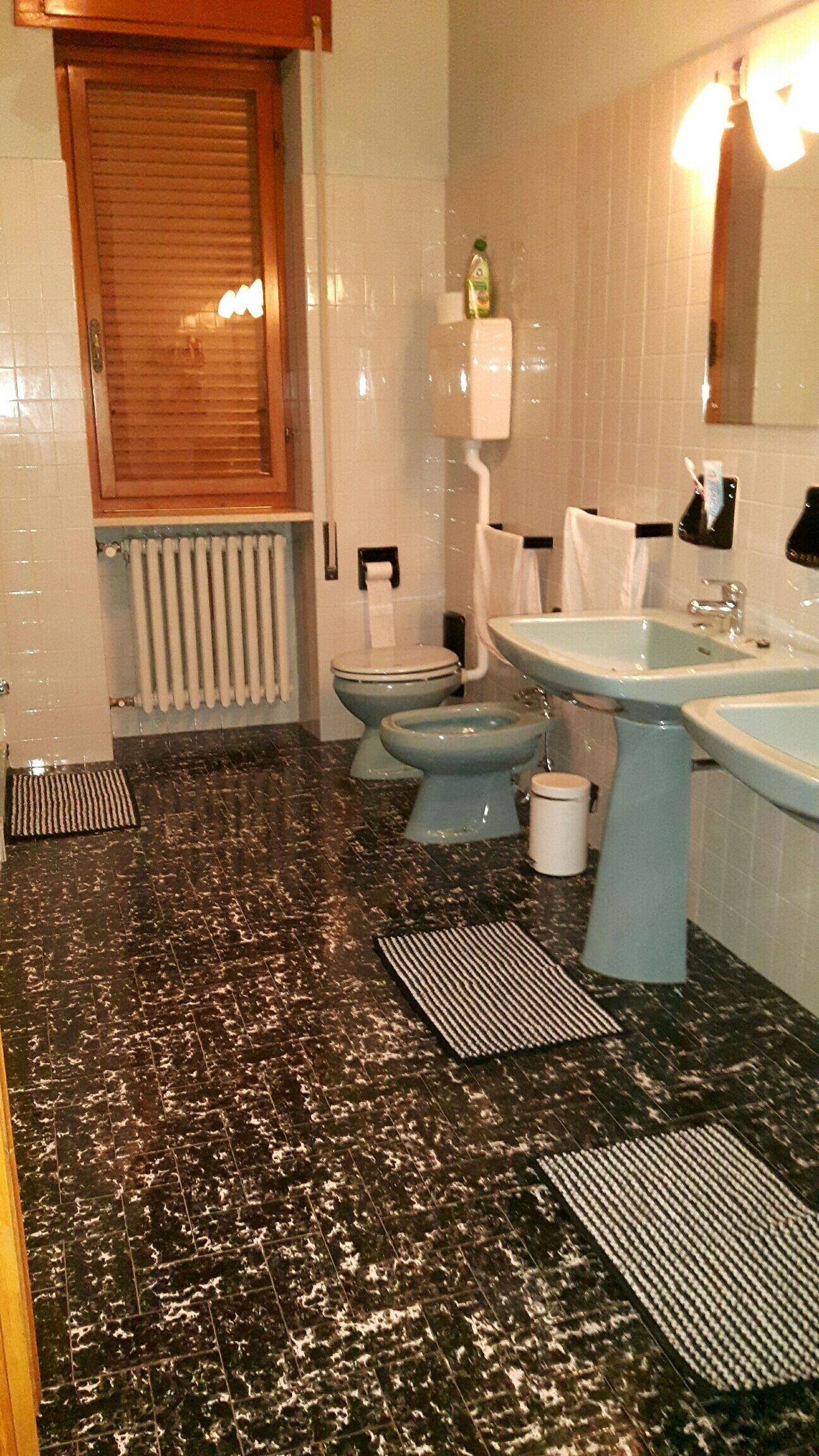 Un baño con piso de mármol, dos inodoros, un lavamanos, un espejo y un radiador.