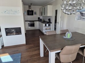 A modern kitchen with white cabinets, a dining area with a wooden table and beige chairs, and a fireplace.