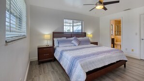 A bedroom with a wooden bed, two bedside tables, a ceiling fan, and a window with blinds. - Villa Sunsplash-Modern, south-facing, large pool- perfect for families (Cape Coral)