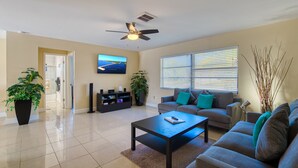 A living room with a sofa, coffee table, and TV. There are potted plants and a ceiling fan. - Villa Sunsplash-Modern, south-facing, large pool- perfect for families (Cape Coral)