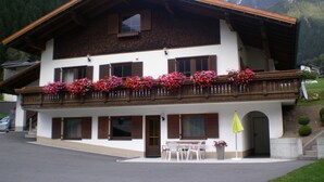 Un bâtiment à deux étages doté d’un balcon orné de fleurs, d’un espace extérieur aménagé et couvert, et offrant une vue sur un paysage montagneux.