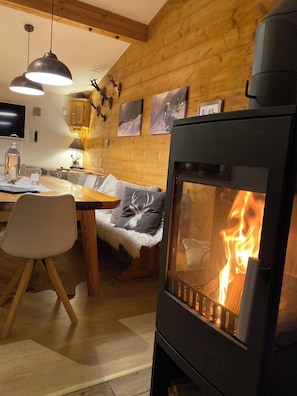 Une pièce chaleureuse avec un poêle à bois, une table à manger avec des chaises, un canapé et un téléviseur fixé au mur.