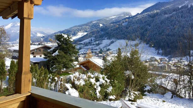 A wooden balcony overlooking a snow-covered village with houses and mountains in the background.