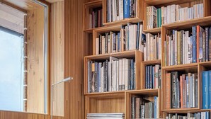 A modern library with wooden bookshelves filled with books, a grey upholstered armchair, and a small wooden side table. - Exclusive design chalet on 1 800 meters, 4-6 pers.,  above Törbel (Törbel)
