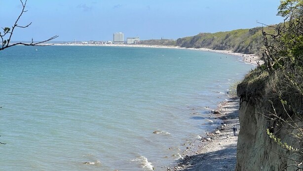 A coastal beach with a rocky shoreline, a cliff, and buildings in the distance. - Exclusive apartment in Warnemünde, 150m to the beach, 2 bathrooms, 2 bedrooms, sauna, WLAN and much more. (Rostock)