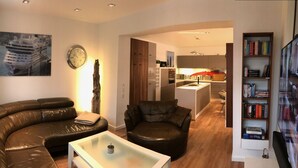 A modern living room with a curved leather sofa, a glass coffee table, and a bookshelf. - Exclusive apartment in Warnemünde, 150m to the beach, 2 bathrooms, 2 bedrooms, sauna, WLAN and much more. (Rostock)