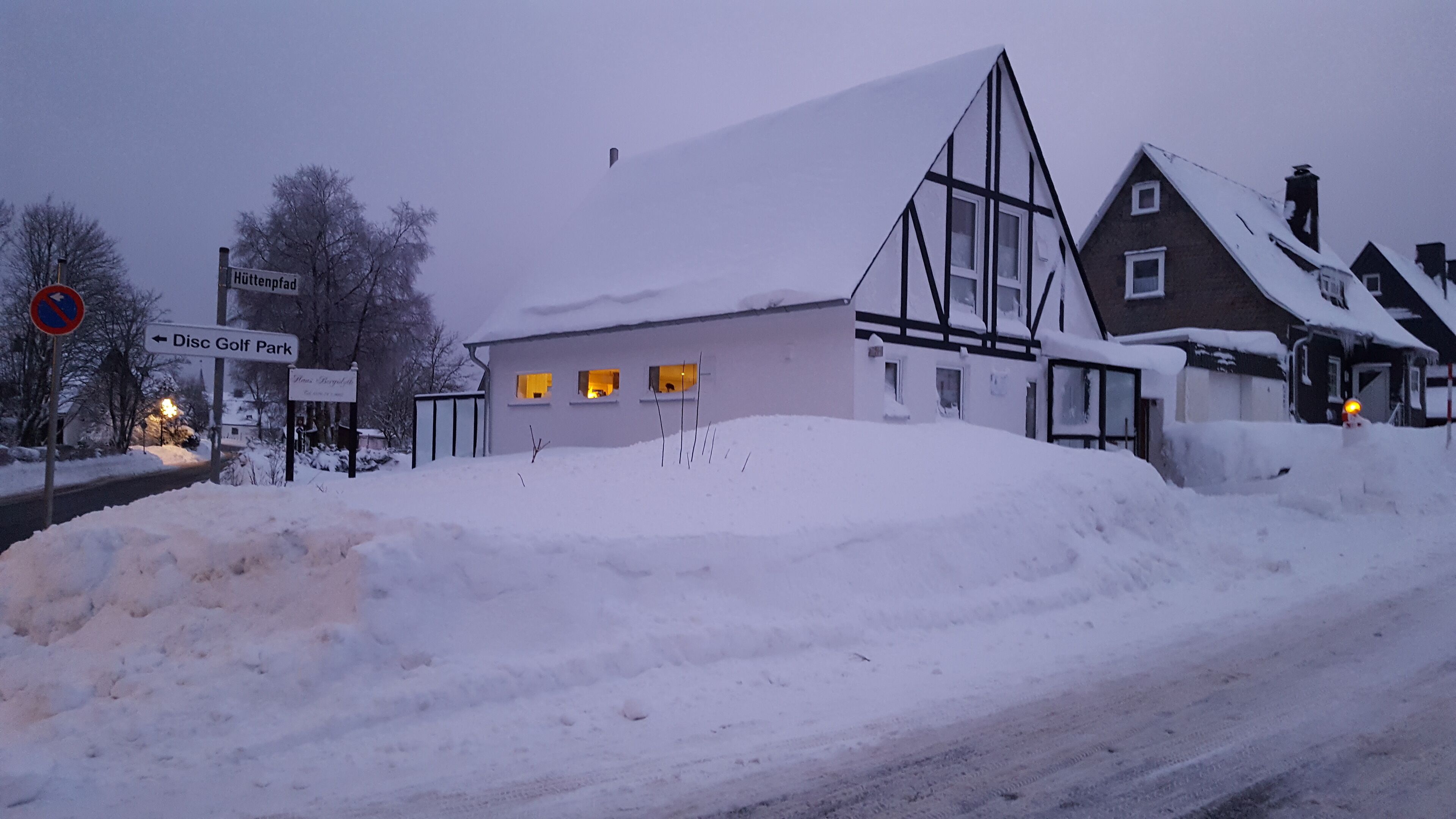A snow-covered landscape with a building that has a triangular roof and a sign indicating a golf course direction.