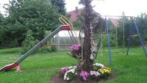 A playground with a slide and swings, surrounded by a garden with various flowers and a tree. - Comfortable house in a quiet location near Meissen  (Nossen)