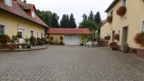 A courtyard with cobblestone paving, two yellow buildings with red-tiled roofs, and potted plants. - Comfortable house in a quiet location near Meissen  (Nossen)