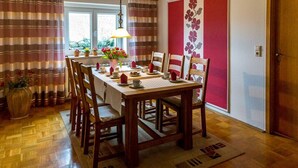 A dining area with a wooden table set for four, surrounded by wooden chairs. There is a vase with flowers on the table, and a lamp hanging above. - Comfortable house in a quiet location near Meissen  (Nossen)