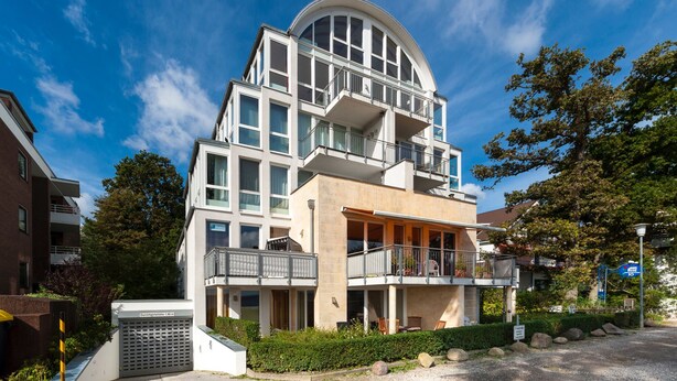 Un bâtiment moderne à plusieurs étages, doté de balcons, d’un espace ext érieur aménagé et couvert, et surplombant un ciel dégagé.