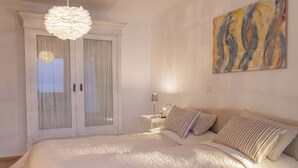 Une chambre à coucher avec un lit, une table de chevet, une lampe, une porte avec des rideaux et un tableau au mur.