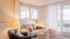 Un salon comprenant un canapé, un fauteuil, deux tables d’appoint, une lampe et un porte-bougie en verre.