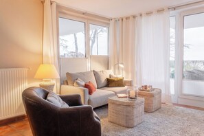 Ein Wohnzimmer mit einer Couch, einem Sessel, zwei Beistelltischen, einer Lampe und einem Glas-Kerzenhalter.