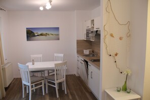 A compact kitchen with white cabinets, a dining table with chairs, and a wall-mounted sink.