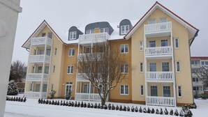 En bygning med flere etager, altaner, snedækket jord og en klar himmel.