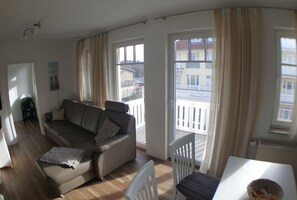 A living room with a sofa, a dining table, and a view of a balcony with a railing.