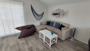 Ein modernes Wohnzimmer mit einer Eckcouch, einem kleinen weißen Tisch, einer Hängematte und einer Heizung.