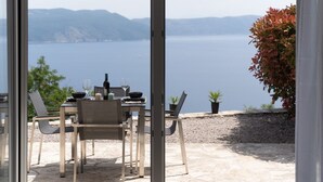 An outdoor dining area with a table set for two, overlooking a body of water and distant mountains. - Apartment with stunning sea views and views of the island of Cres (Mali Kosi)