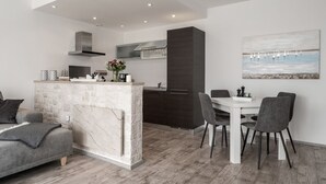 A modern kitchen with a central island, dark cabinetry, and a dining area with a white table and grey chairs. - Apartment with stunning sea views and views of the island of Cres (Mali Kosi)
