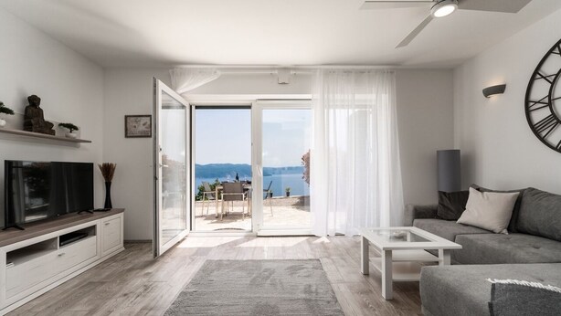 A modern living room with a flat-screen TV, a sofa, a coffee table, and a view of the outdoors. - Apartment with stunning sea views and views of the island of Cres (Mali Kosi)