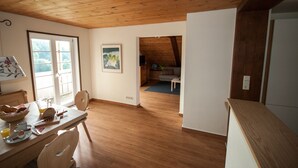 Een ruime kamer met houten vloeren, een eethoek met een ontbijtstafel, en een gezellige zithoek met een bank en een lamp.
