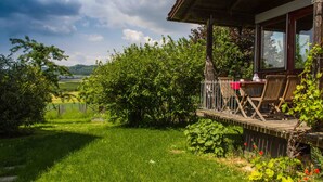 A wooden deck with outdoor furniture, surrounded by lush greenery and a view of a distant landscape. - Pure relaxation! Holiday home: integrated into the nature with modern interior! (Frickingen-Altheim)