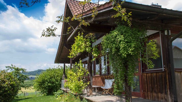 A wooden cabin with a porch, a chair, and a view of the countryside. - Pure relaxation! Holiday home: integrated into the nature with modern interior! (Frickingen-Altheim)