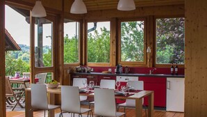 A wooden cabin with a dining area, kitchen, and large windows offering a view of the outdoors. - Pure relaxation! Holiday home: integrated into the nature with modern interior! (Frickingen-Altheim)