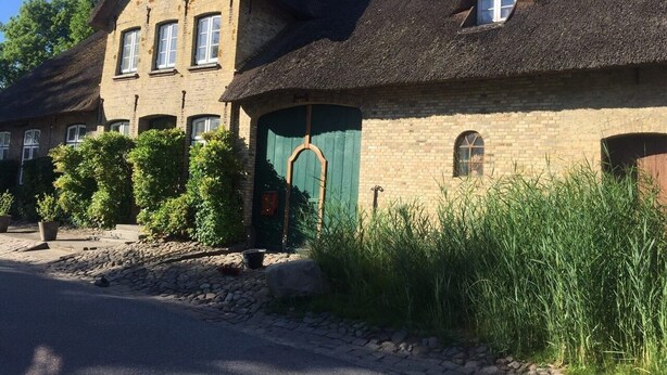 En traditionell byggnad i tegel med ett halmtak, en grön dörr och ett litet fönster.