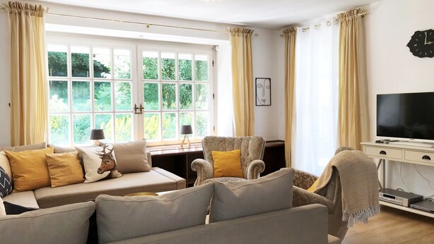 A living room with a sofa, armchairs, a television, and a window with curtains.