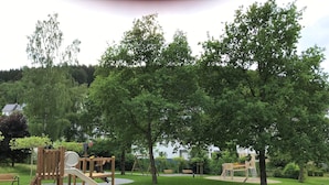 A playground with a slide, climbing structures, and sand area, surrounded by trees and grass.